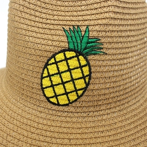 Détail de la texture tressée en paille et broderie d'ananas colorée sur le chapeau