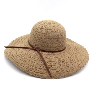 Detail of hollow woven straw sun hat featuring a wide brim and slim brown leather bow