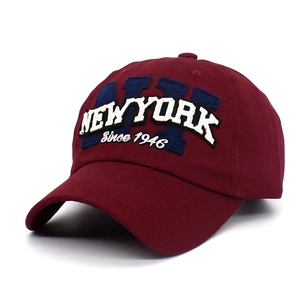 Detailed close-up of white NY embroidery on a wine red cotton baseball cap with curved brim