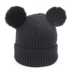 Detail of black knit beanie featuring two large faux fur pom-poms and ribbed cuff texture