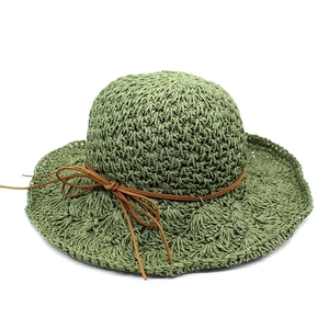 Detail of hand-woven olive green raffia sun hat with brown leather bow and wavy brim