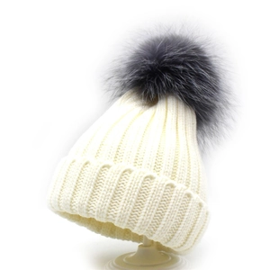 Close-up of knit texture and fluffy dark grey pompom on cream winter beanie hat