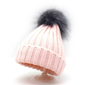 Close-up of knit texture and gray faux fur pom-pom on a pink winter knit beanie