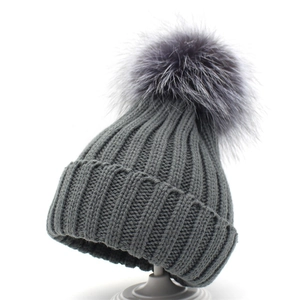 Close-up of thick ribbed knit texture and large fluffy faux fur pompom on grey winter hat