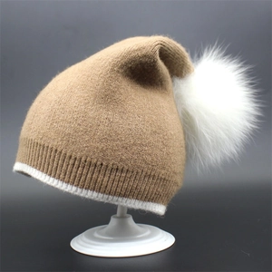 Macro detail of khaki knit beanie with fluffy white faux fur pom-pom and ribbed edge