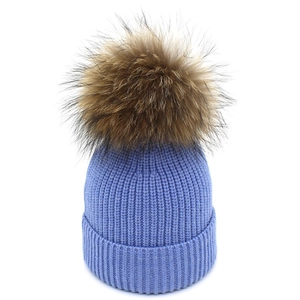 Dettaglio del cappello in maglia azzurro con un pompon in pelliccia sintetica marrone soffice