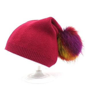 Dettaglio del berretto in maglia rosa acceso con un pompon multicolore in ecopelliccia