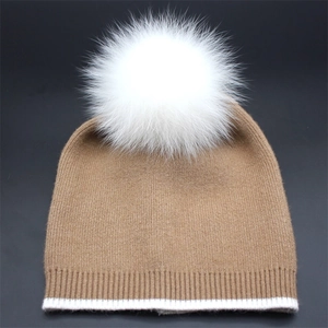 Close-up of knit texture on camel beanie with white stripes and fluffy faux fox fur pom