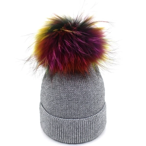 Détail d'un bonnet en maille côtelée grise avec un grand pompon en fourrure multicolore