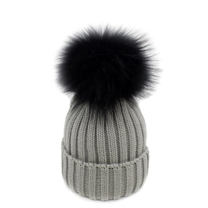 Dettaglio del cappello in maglia grigio con trama a coste e grande pompon nero in ecopelliccia