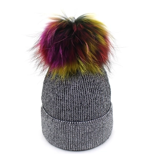 Détail d'un bonnet en tricot argenté avec un grand pompon multicolore en fausse fourrure