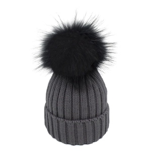 Dettaglio del berretto in maglia grigio scuro con pompon nero e trama a coste spesse