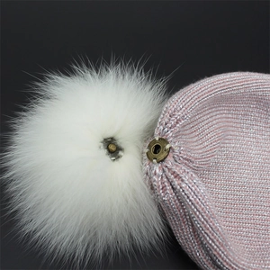 Detailed close-up of a pink knit beanie featuring a detachable fluffy white faux fur pompom