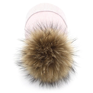 Pink knit winter hat with large raccoon fur pompom shown on white background