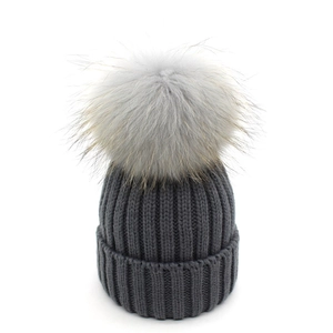 Dettaglio del berretto in maglia grigio scuro con un grande pompon di pelliccia grigia