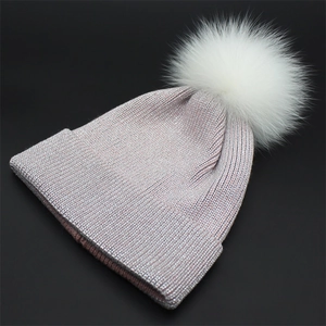 Detailed close-up of pink knit beanie with silver shimmer threads and white fur pompom