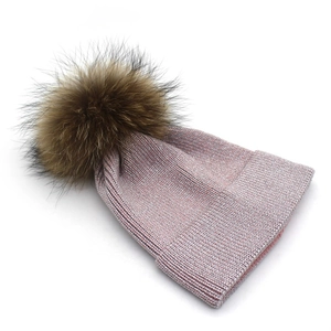 Macro shot of light pink knitted beanie featuring sparkling metallic thread and faux fur pom-pom