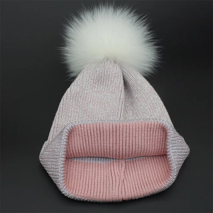 Close-up of pink knit hat with silver glitter thread and a large fluffy white fur pom-pom
