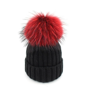 Berretto invernale in maglia nera da donna con un grande pompon rosso decorativo soffice
