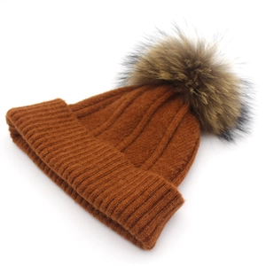 Detail of camel brown knitted winter hat with fluffy raccoon fur pompom and ribbed texture