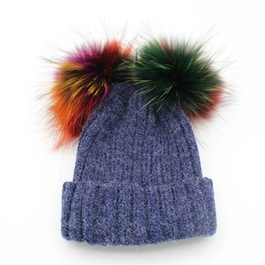 Close-up of chunky navy blue knit beanie with two oversized colorful faux fur pom-poms