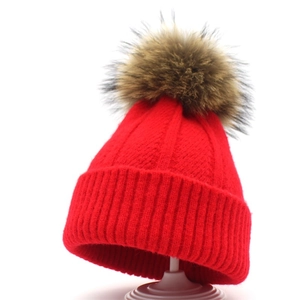 Deep red knitted winter beanie for women with large fluffy faux fur pompom on white background