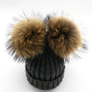 Detalle de gorro de punto gris oscuro con dos pompones grandes de piel sintética