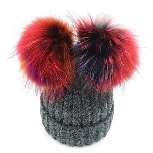 Women's grey knit beanie with two colorful raccoon fur pom-poms on a white background