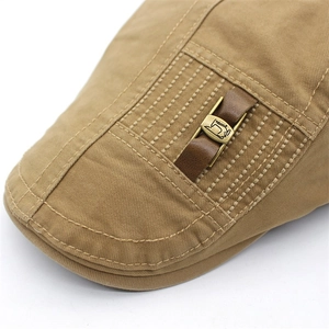 Detail of khaki cotton flat cap featuring brown leather strap and bronze metal buckle
