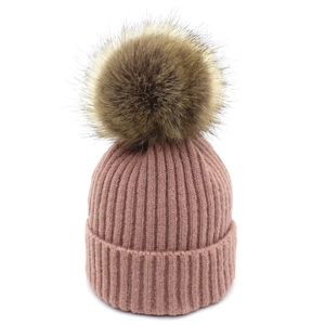 Détail du bonnet en maille côtelée rose poudré avec un grand pompon en fausse fourrure douce
