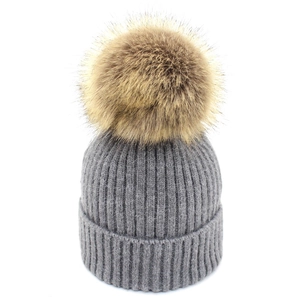 Détail du tricot d'un bonnet gris avec un grand pompon en fausse fourrure moelleuse
