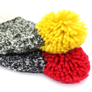 Detail of multi-color thick knit wool hat with vibrant yellow and red oversized pom-poms
