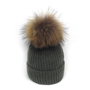Detaillierte Nahaufnahme der dunkelgrünen Strickmütze mit flauschigem braunem Kunstfell-Bommel