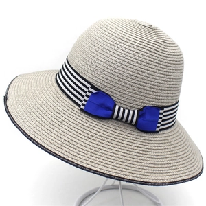 Close-up of woven straw sun hat with striped ribbon and blue bow detail on white stand
