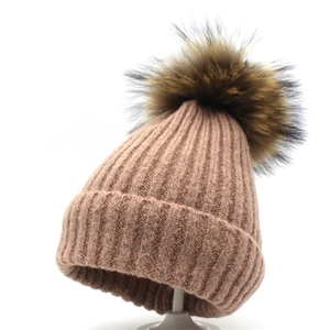 Detail einer rosa Winterstrickmütze mit Rippmuster und flauschigem braunem Pelzbommel
