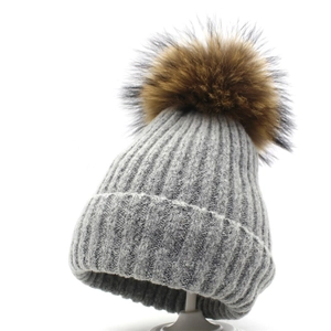 Detailansicht der grauen Strickmütze mit flauschigem braunem Pelzbommel und Rippenmuster