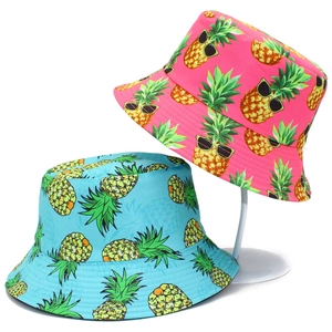 Pink and blue reversible bucket hats with cartoon pineapple prints on white stands