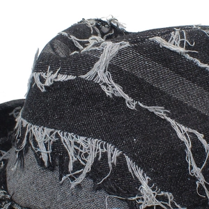 Detailed close-up of distressed denim hat fabric with shredded holes and punk fringe edges