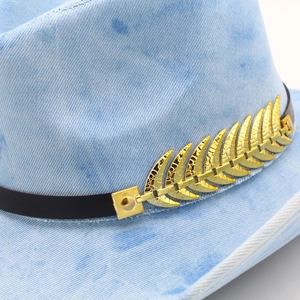 Close-up of light blue denim fedora featuring brown leather band and gold leaf buckle