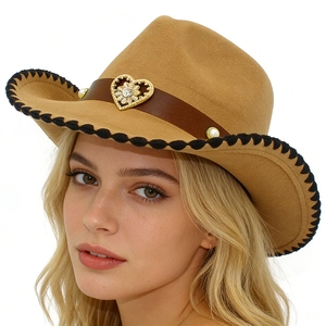 Dettaglio cappello cowboy in feltro con fibbia a cuore, perle e bordo a pompon