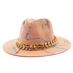 Straw Panama hat in peach pink with colorful paint splatters and a bold gold chain link