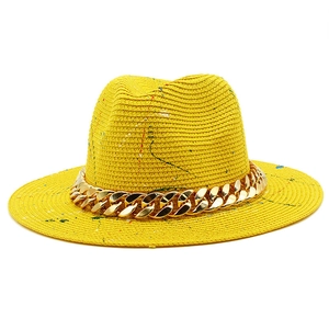 Detail of yellow straw fedora with colorful paint splatters and bold gold chain