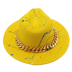Detail of yellow fedora straw hat with colorful graffiti paint and thick gold chain link