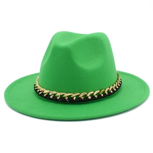 Détail d'un chapeau fedora en laine vert vif avec une grosse chaîne décorative or et noir