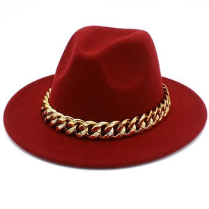 Detail view of dark red fedora hat with a bold gold chain band on white background