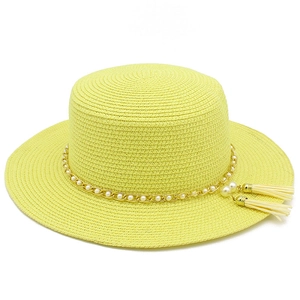 Dettaglio di un cappello di paglia giallo con catena dorata e nappe di perle eleganti