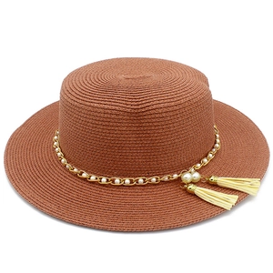 Dettaglio cappello di paglia con catena dorata, perle bianche e nappe beige