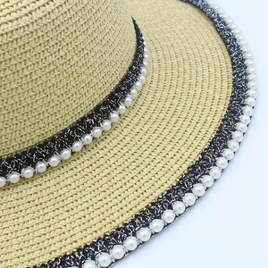 Detail of woven straw hat featuring black band with white pearls and fine craftsmanship