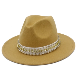 Détail d'un chapeau fedora en laine camel avec ruban blanc, rivets et strass jaunes brillants