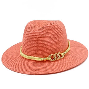 Detail of coral orange woven straw fedora hat featuring a stylish gold chain buckle